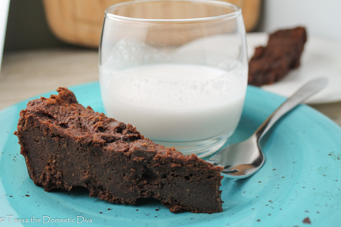 a triangle cut slice of vegan chocolate brownies on a blue plate with a cup of milk