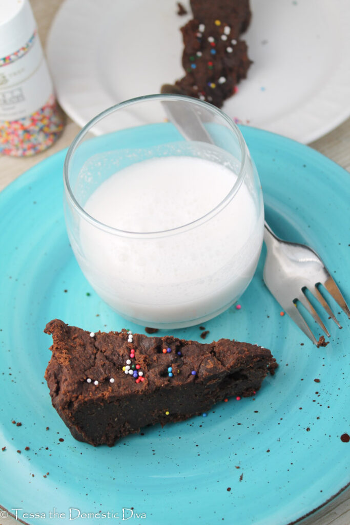 overhead view of a triangle slice of a dense chocolate brownies on a blue plate with rainbow sprinkles