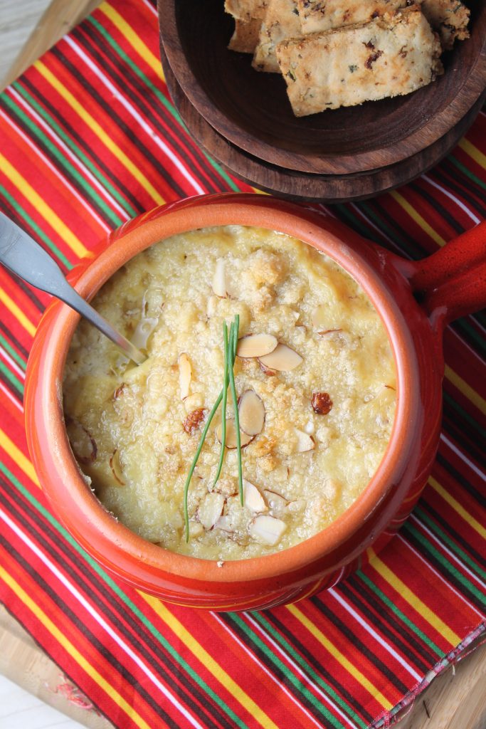 overhead look at a golden brown and crisped hot artichoke dip with an almond topping and homemade almond crackers in the background