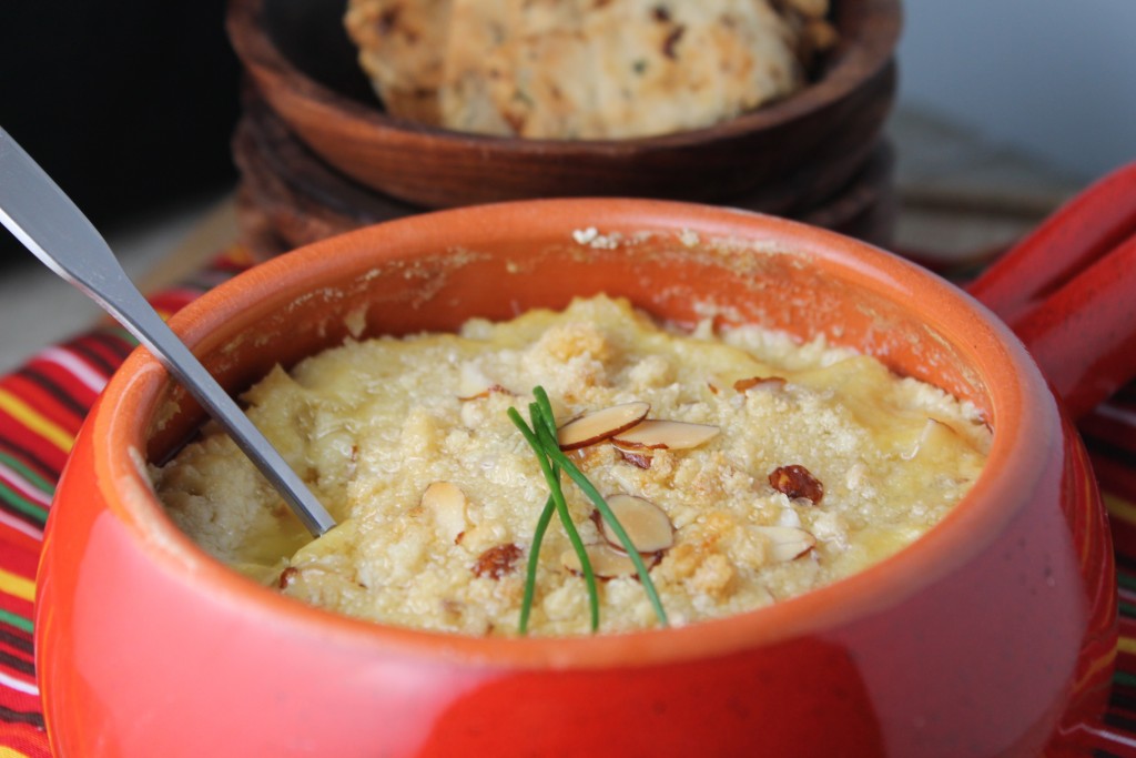 bowl filled with a bubbling hot artichoke dip topped with almonds and a sprig of chives