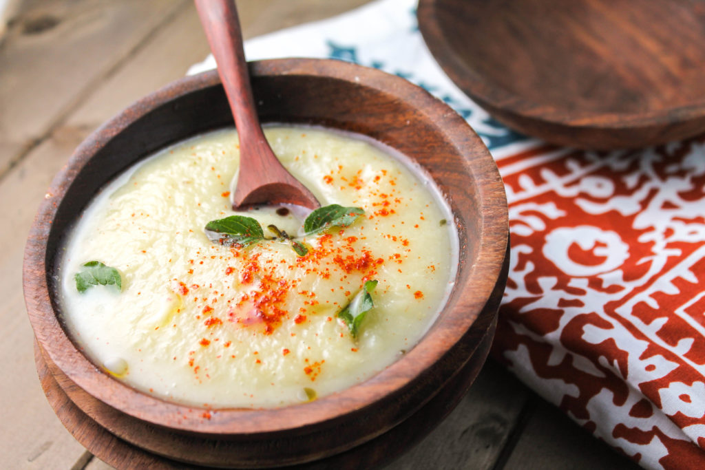 dark wooden bowl filled with a creamy white soup garnished with olive oil and oregano leaves