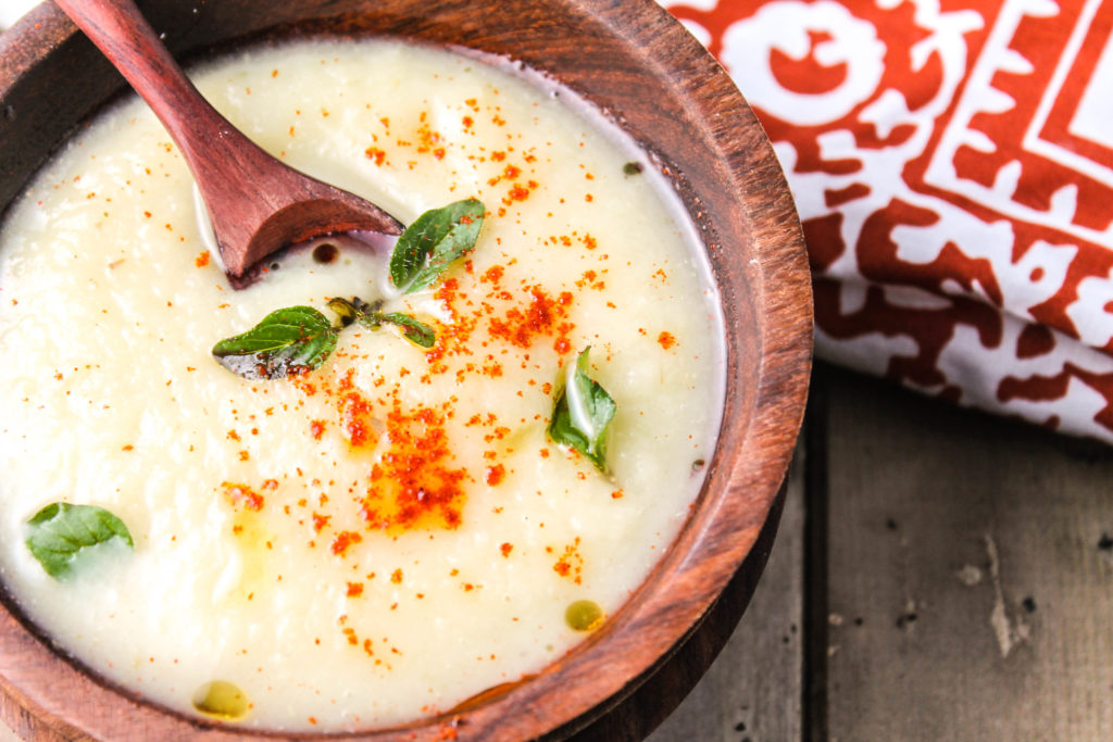 wooden bowl filled with a creamy white soup with fresh oregano leaves as a garnish