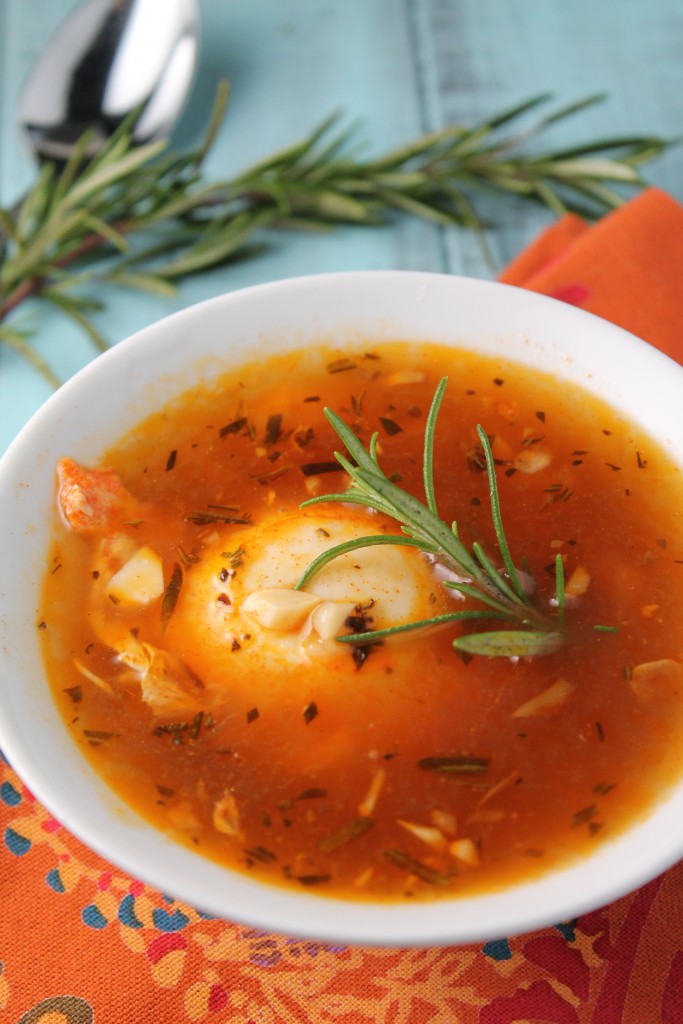 a poached egg floating in a orange hued broth with a garnish of fresh rosemary