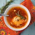 birds eye view of a white bowl filled with a rich orangish red broth with a poached egg and fresh rosemary