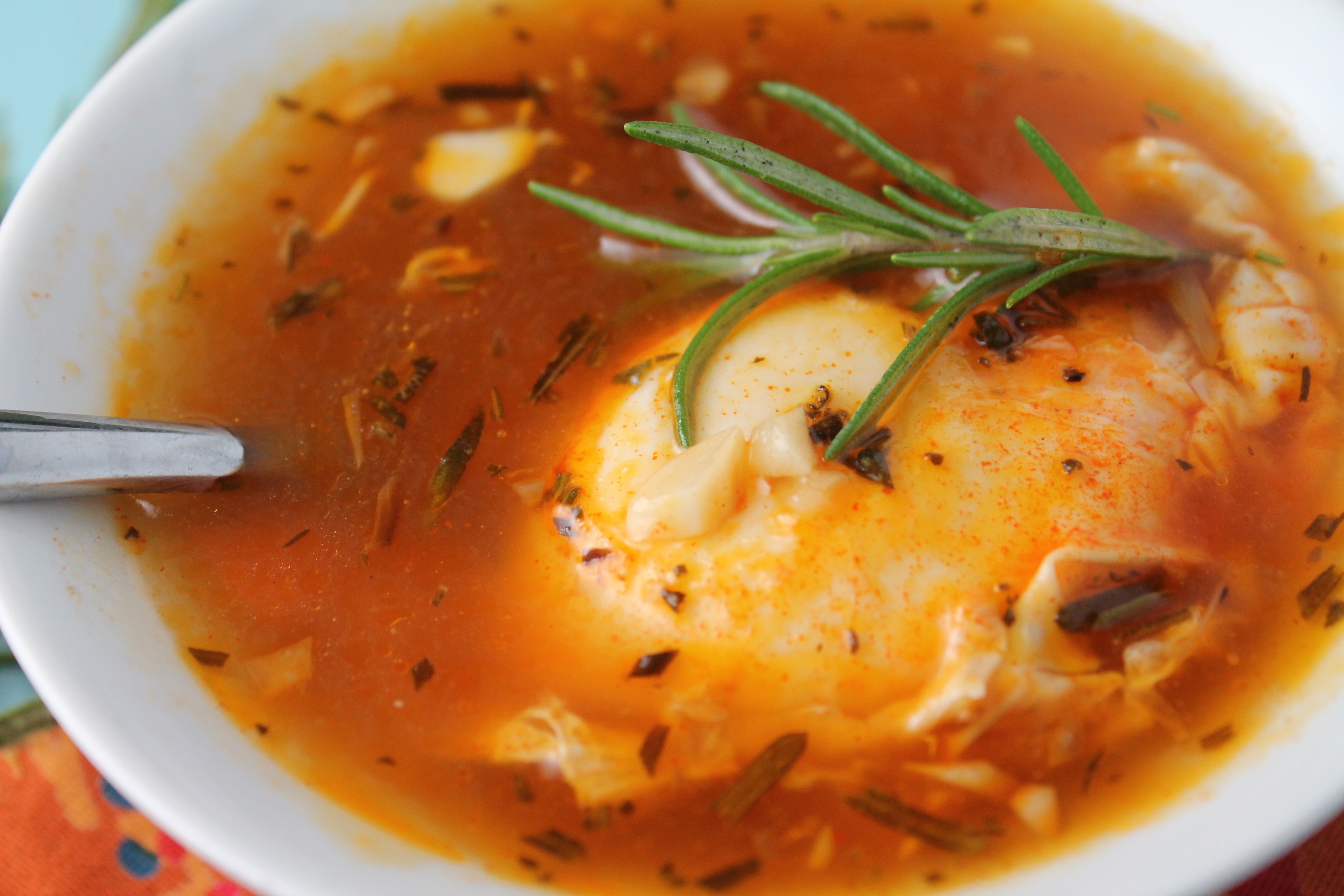 overhead shot of a perfectly poached egg floating in a orange red smoked paprika broth and a garnish of fresh rosemary