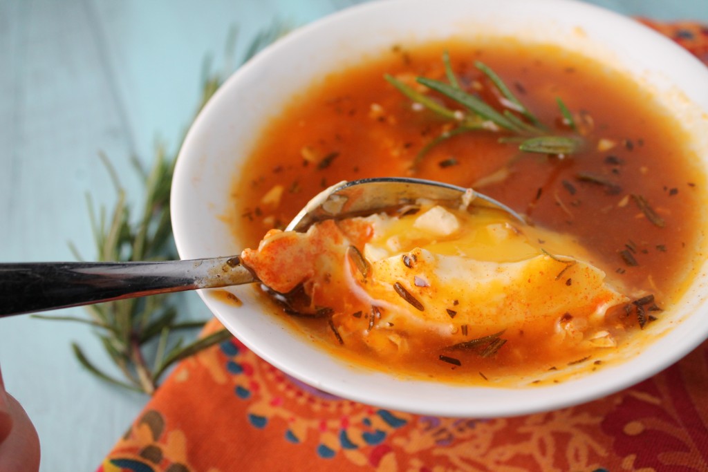 close up of a white bowl filled with orange hued broth with a molten poached egg and rosemary