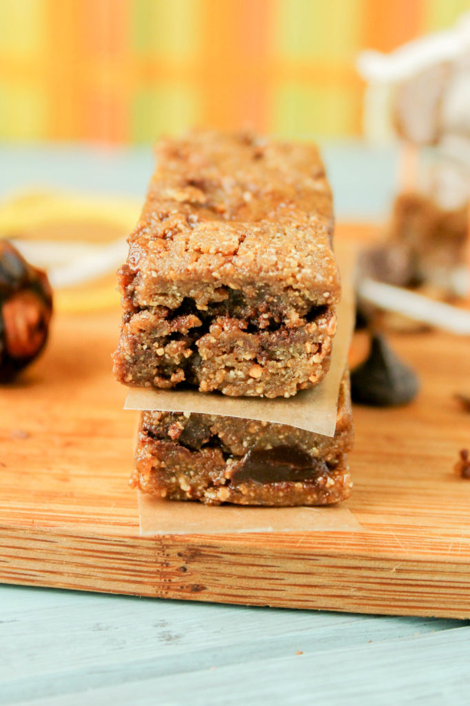 2 rectangular nut and date bars with chocolate chips separated by a piece of parchment on a bamboo cutting board at eye level