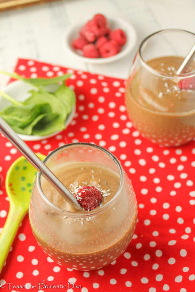 two clear glasses filled with a creamy chocolate smoothie with avocado spinach and fresh raspberries