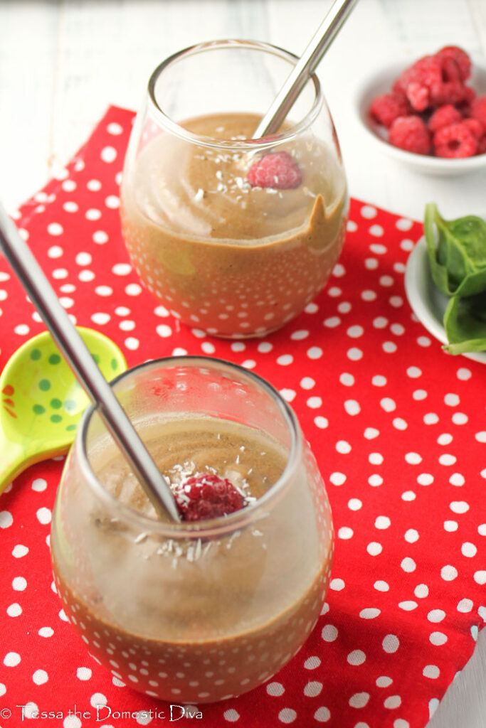 two glass on a red cloth filled with a healthy chocolate raspberry shake with baby greens and stainless steel straws