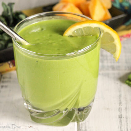 a clear class with a thick and creamy green smoothie with mango and lemon and coconut