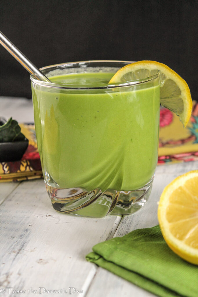 eye level view of a clear glass with reusable straw and filled with thick and creamy green mango smoothie with a lemon slice