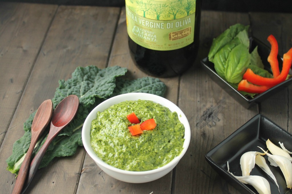 leafy green dairy free kale in a white bowl on a dark wood surface with fresh basil, red bell peppers, garlic, and kale leaves