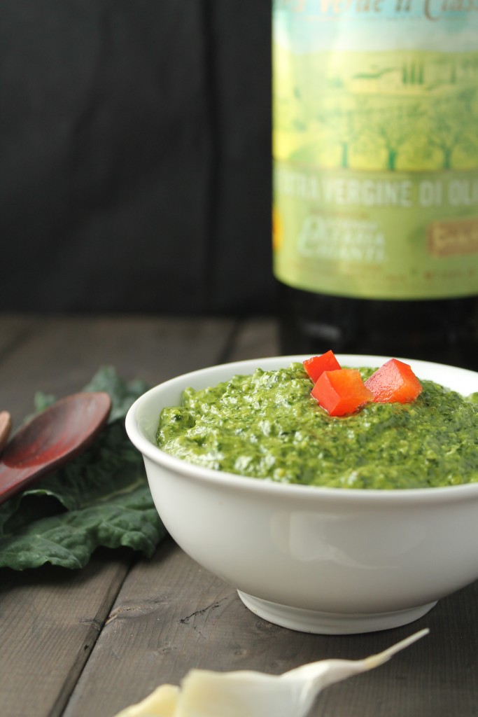 eye level image of a creamy bright green pesto with a cherry red pepper garnish on a dark wood surface