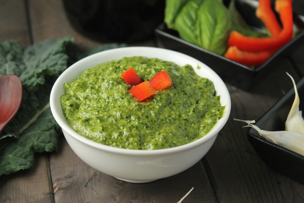 bright green pesto in a white bowl topped with diced red pepper on a dark wooden surface