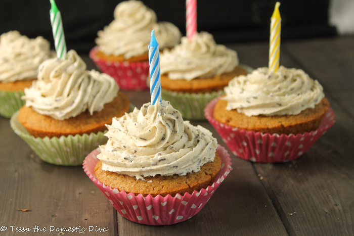 six vanilla cupcakes topped with swirled vanilla speckled frosting in a swirled pattrn with a single birthday candle in each