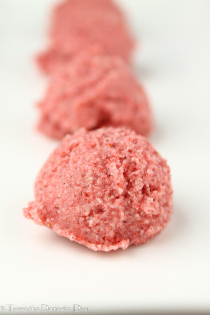 a close up view row of several raw pink hued starwberry macaroons on a white plate