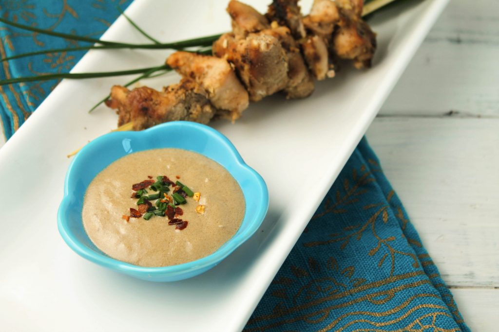 a blue dipping dish with Thai peanut sauce and a chicken skewer.