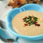 vertical close up of a creamy peanut sace in a small turquosie dipping bowl with a garnish of chives and red pepper flakes