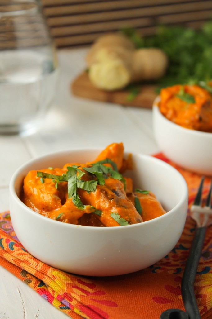 dairy free chicken tikka masala in a white bowl on a festive deep pumpkin orange paisley cloth