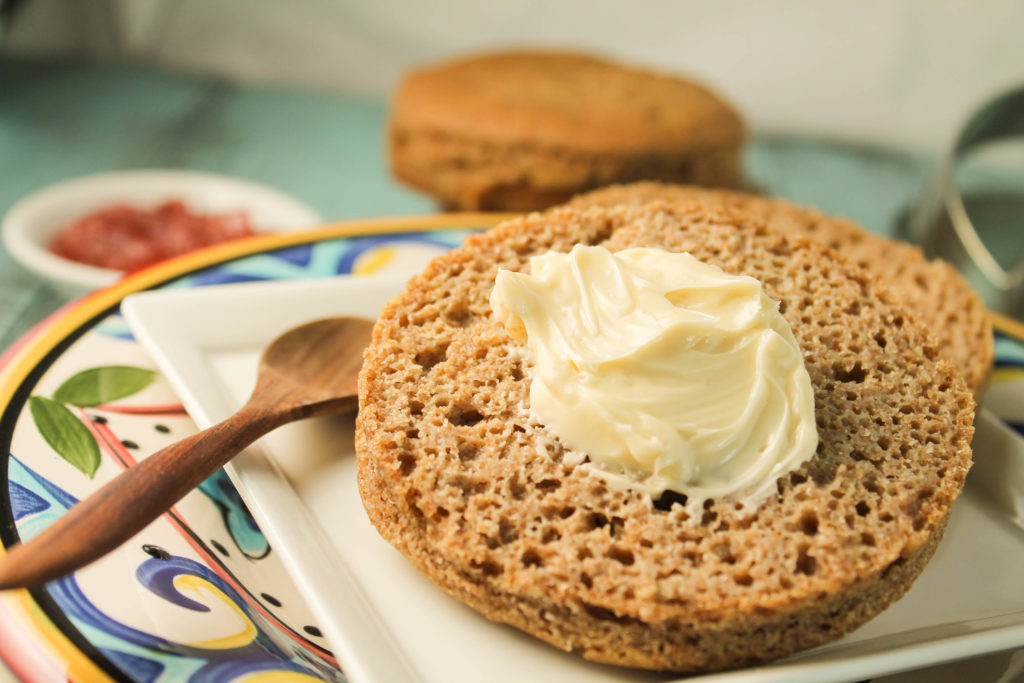 sliced gluten free vegan English muffins of soaked teff bread on a white square plate with a dollop of softened butter