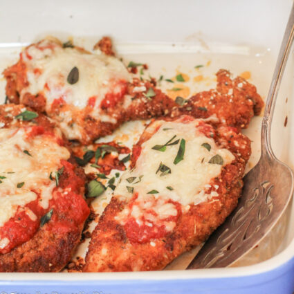 chicken parmesan no egg in blue ceramic baking dish with tomatoe sauce and melted cheese