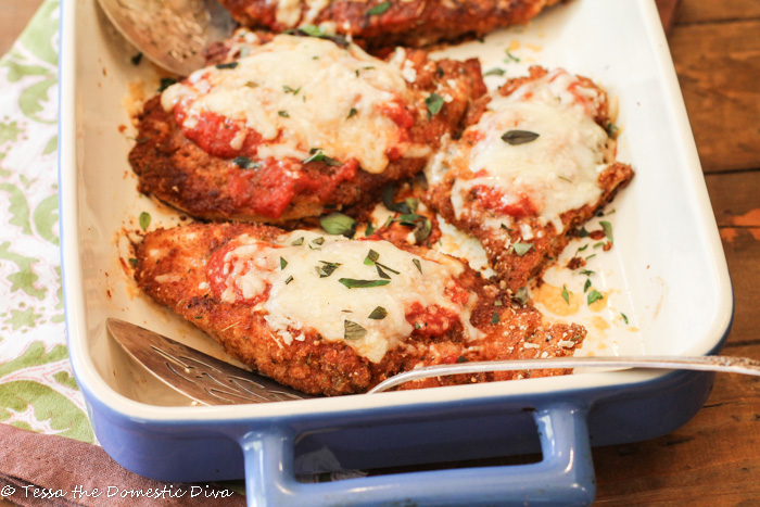 a blue and white ceramic baking dish with breaded cutlets of chicken breast topped with spaghetti sauce and melted dairy free cheese