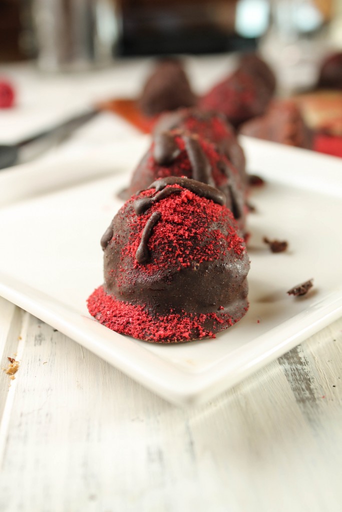 vertical image of 3 raspberry dusted chocolate truffles on a white plate on a light wooden surface