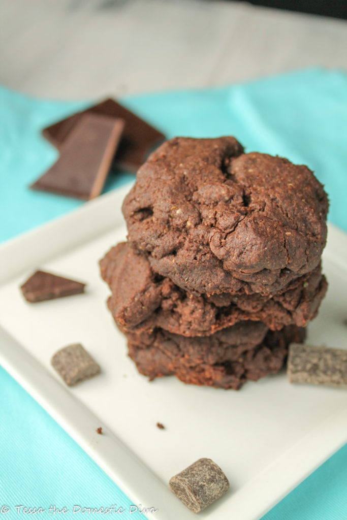 three chococlate chococlate chip cookies stacked on a white plate with chocolate chunks