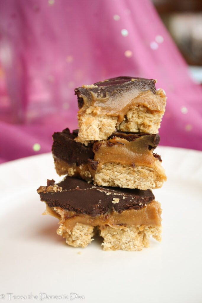 three bars of chocolate peanut butter bars on white plate with purple background