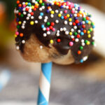 chocolate covered cookie dough ball on a white and blue striped paper straw with sprinkles