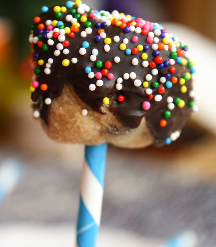 chocolate covered cookie dough ball on a white and blue striped paper straw with sprinkles