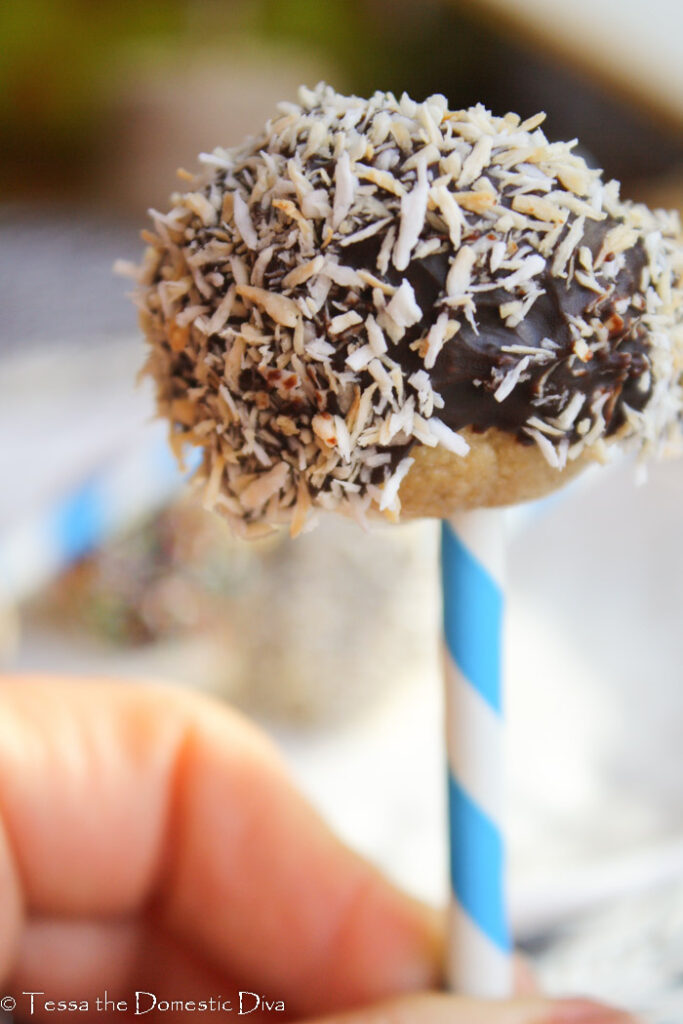 a toasted coconut chocolate covered cookie dough pop on a paper straw
