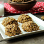 a square white plate of 4 oatmeal cookies with raisins a a glass of milk