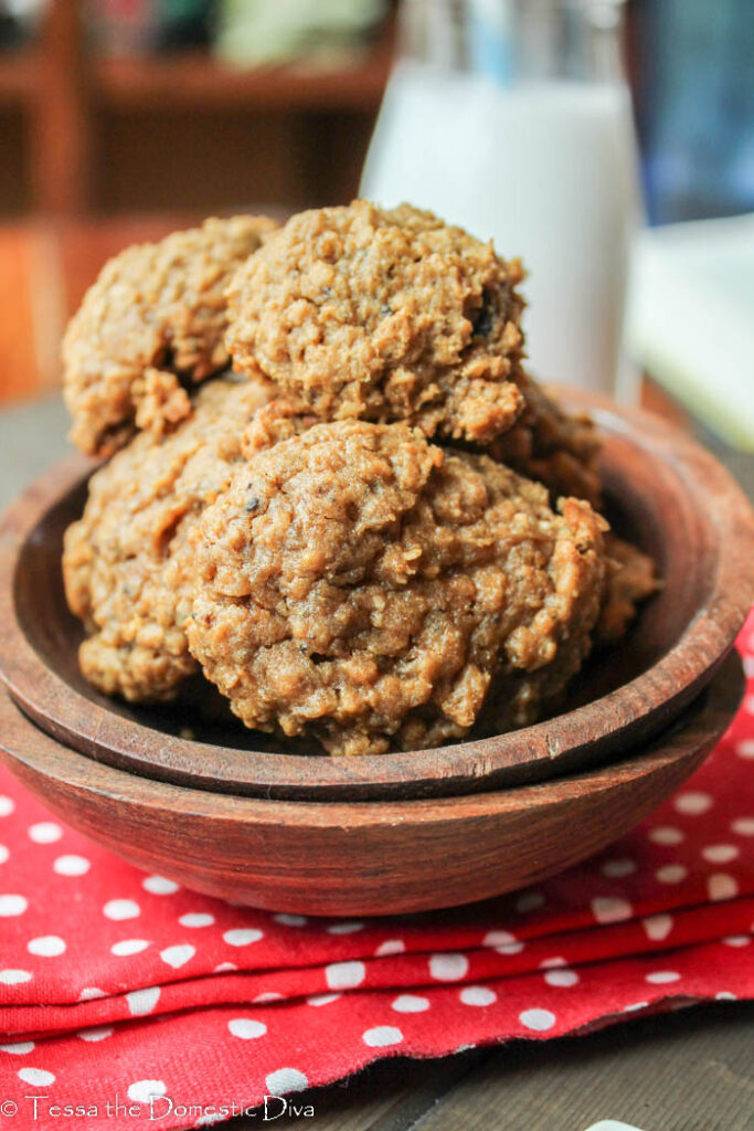 two stacked wooden bowls filled with cinnamon and raisin oatmeal cookies on a red cloth with a glass of milk