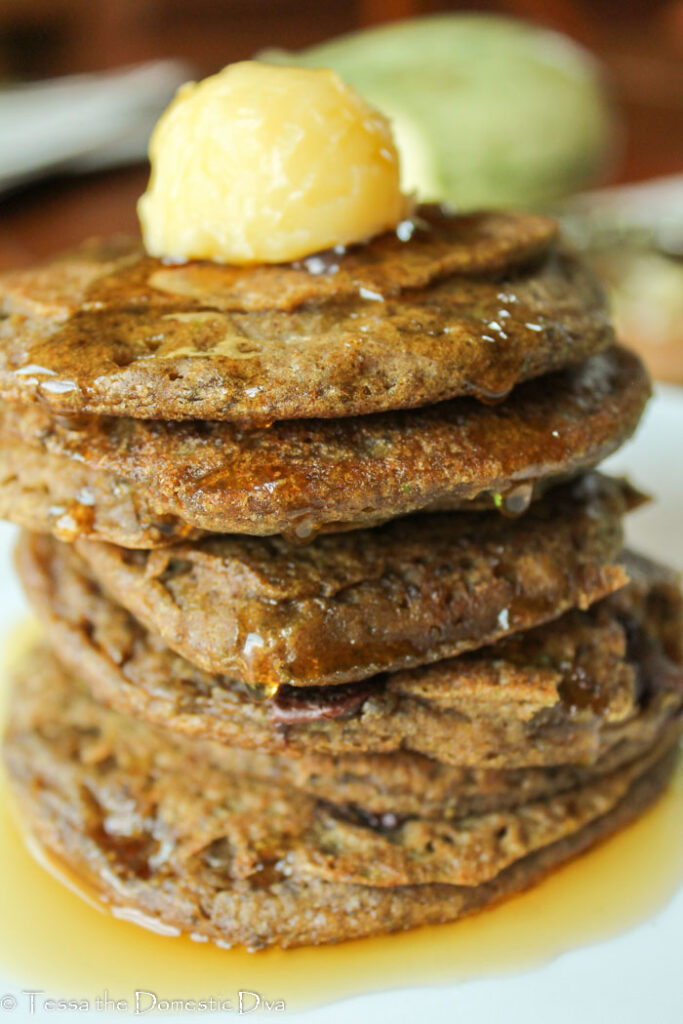 a stack of zucchini pancakes on a white plate with chocolate chips and a scoop of butter