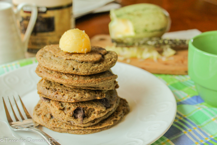 eye level stack of 5 golden brown chocolate chip studded pancakes on a white plate and a dollop of yellow hued butter