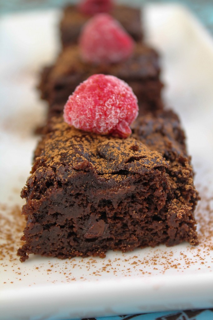 front clode up of thre squares of gluten free vegan chocolate cake dusted with cocoa powder and topped with a raspberry