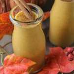 2 vintage glasses filled with a creamy pumpkin smoothie with a cinnamon stick and fall leaves scattered about