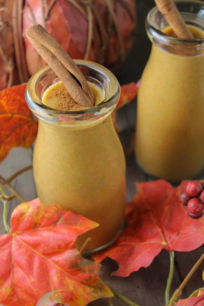 2 vintage glasses filled with a creamy pumpkin smoothie with a cinnamon stick and fall leaves scattered about