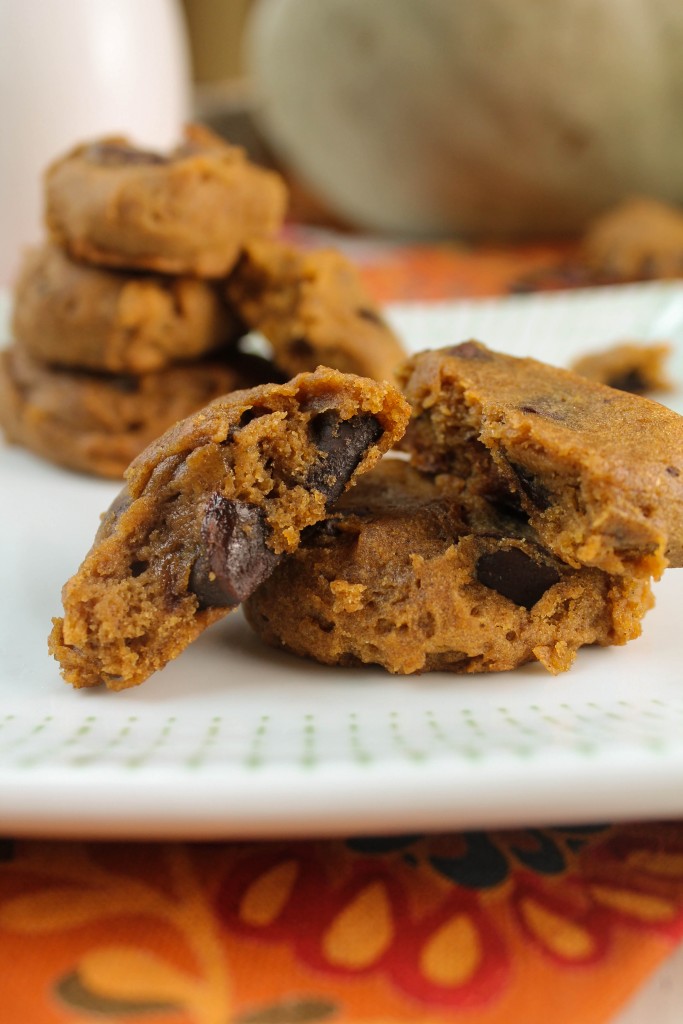 vertical image of soft ornage hued pumpkin cookies studded with chocolate chips from eye level on a white plate atop a fall colored linen