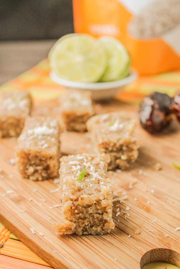 rectangle squares of nut, coconut, date, hemp, and lime bars atop a bamboo cutting board.