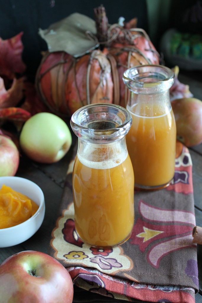 two clear glasses filled with froth apple cider and pumpkin