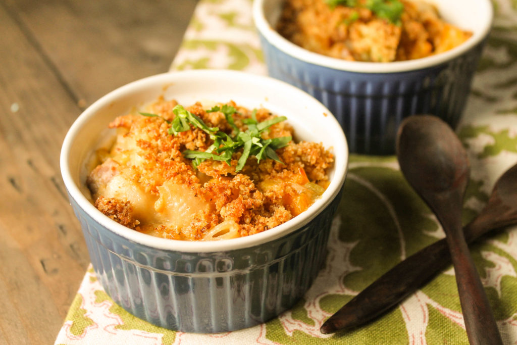 two blue ramekins filled with creamy tuna noodles topped with a crunchy topping on a dark wood surface 