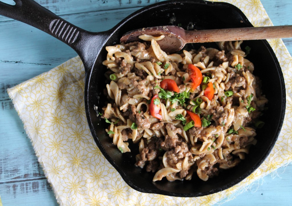 birds eye view of a cast iron skillet with hamburger helper style ground beef and noodle dish with diced tomato and fresh parsley