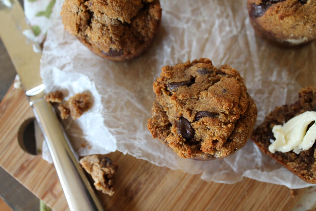 overhead view of several chocolate chip style muffins atop a bamboo cutting board and crumpled parchment paper