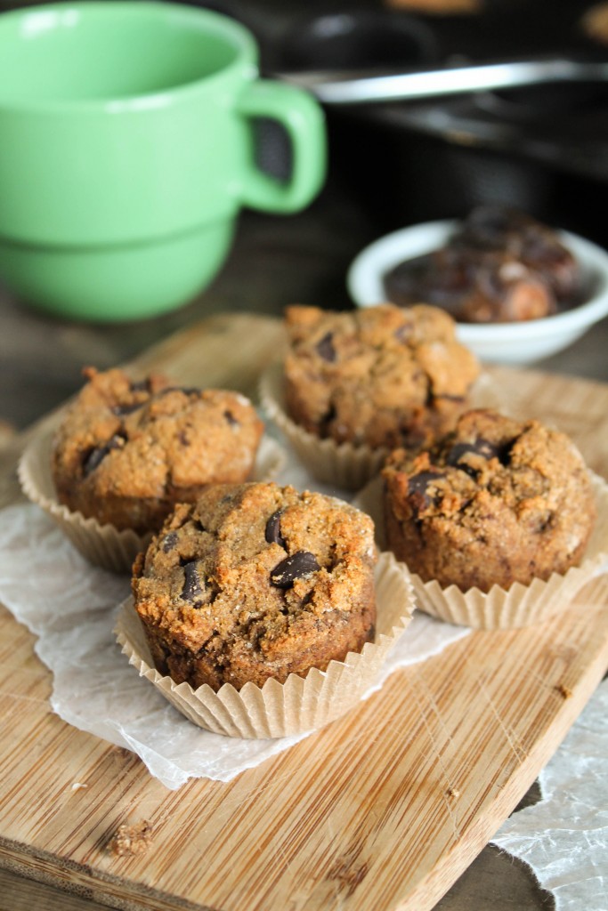 4 mini sweet potato muffins with chocolate chips atop a bamboo cutting board with green coffee mug