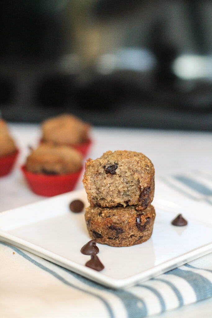 paleo Banana muffins stacked and cut in half on a white plate with a white and pale blue cloth