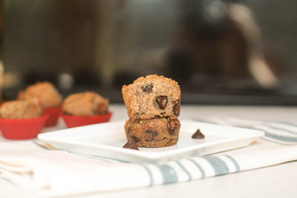 two halves of a banana muffin stacked on a white and blue cheesecloth with mini muffin in background