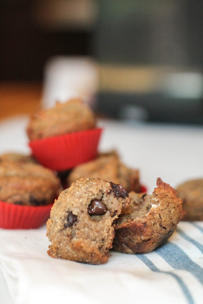serveral mini banana muffins in red silicon liners with chocolate chips arranged on a cheesecloth