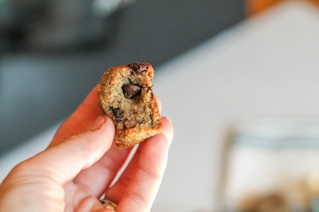 hand held torn piece of a dense banana muffin with melty chocolaty chips